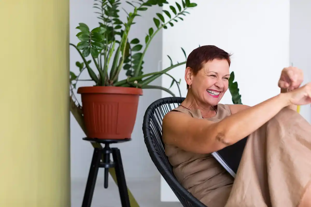 happy mature woman watering indoor plants sunny livingroom Czech home